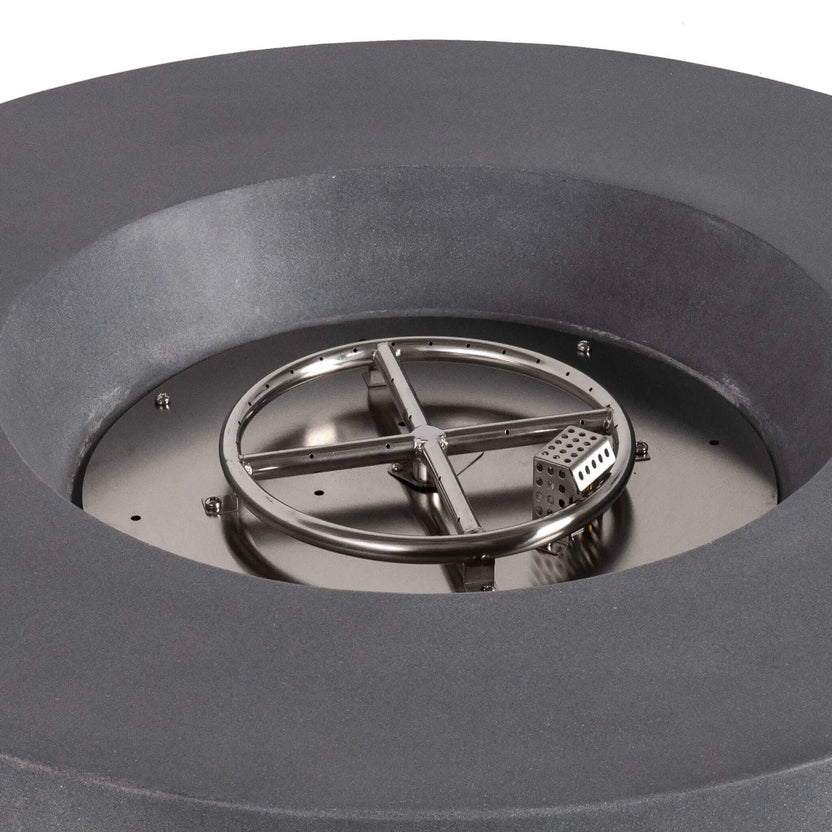 Close-up of the stainless steel circular burner and integrated CSA-certified ignition system inside the Flame Havens Refuge Series 43-inch Round Propane Gas GFRC Concrete Fire Pit in Gray. The image showcases the precision burner ring, ignition cage, and premium stainless steel components before black reflective fire glass is installed.