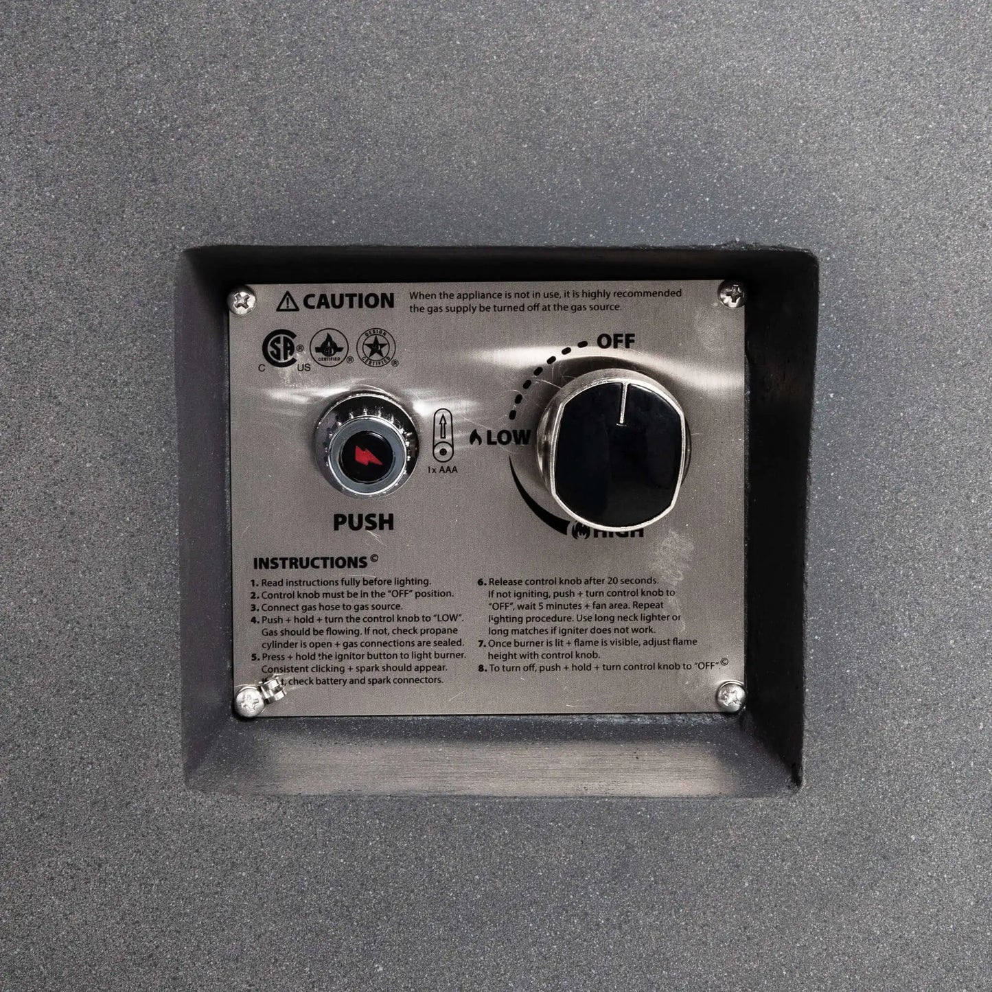 Close-up of the recessed CSA-certified ignition and control panel on the Flame Havens Refuge Series 43-inch Round Propane Gas GFRC Concrete Fire Pit in Gray. The stainless steel control plate features the electronic igniter, flame adjustment knob, operating instructions, and safety markings for reliable propane fire pit operation.