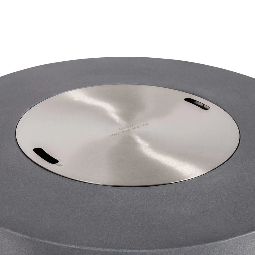The Flame Havens Refuge Series 43-inch Round Propane Gas GFRC Concrete Fire Pit in Gray featuring the optional stainless steel burner cover installed flush within the burner opening. The brushed stainless steel cover creates a clean tabletop surface while protecting the burner system when the fire pit is not in use, complementing the modern GFRC concrete design.