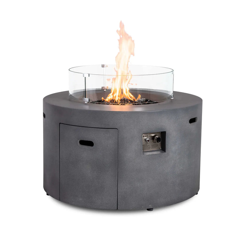 The Flame Havens Refuge Series 43-inch Round Propane Gas GFRC Concrete Fire Pit in Gray operating with premium black reflective fire glass and the optional tempered glass wind guard installed. The transparent wind guard surrounds the flame while providing protection from wind and preserving clear views of the fire from every angle.