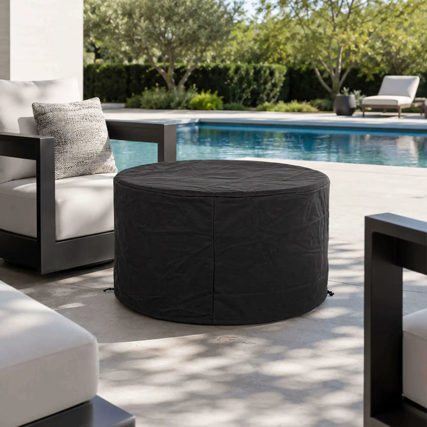 Lifestyle image of the Flame Havens Refuge Series 43-inch Round Propane Gas GFRC Concrete Fire Pit in White protected by the optional black weather-resistant fabric cover. Positioned beside a modern swimming pool and luxury outdoor seating, the cover helps safeguard the fire pit from the elements while maintaining a clean, refined appearance when not in use.