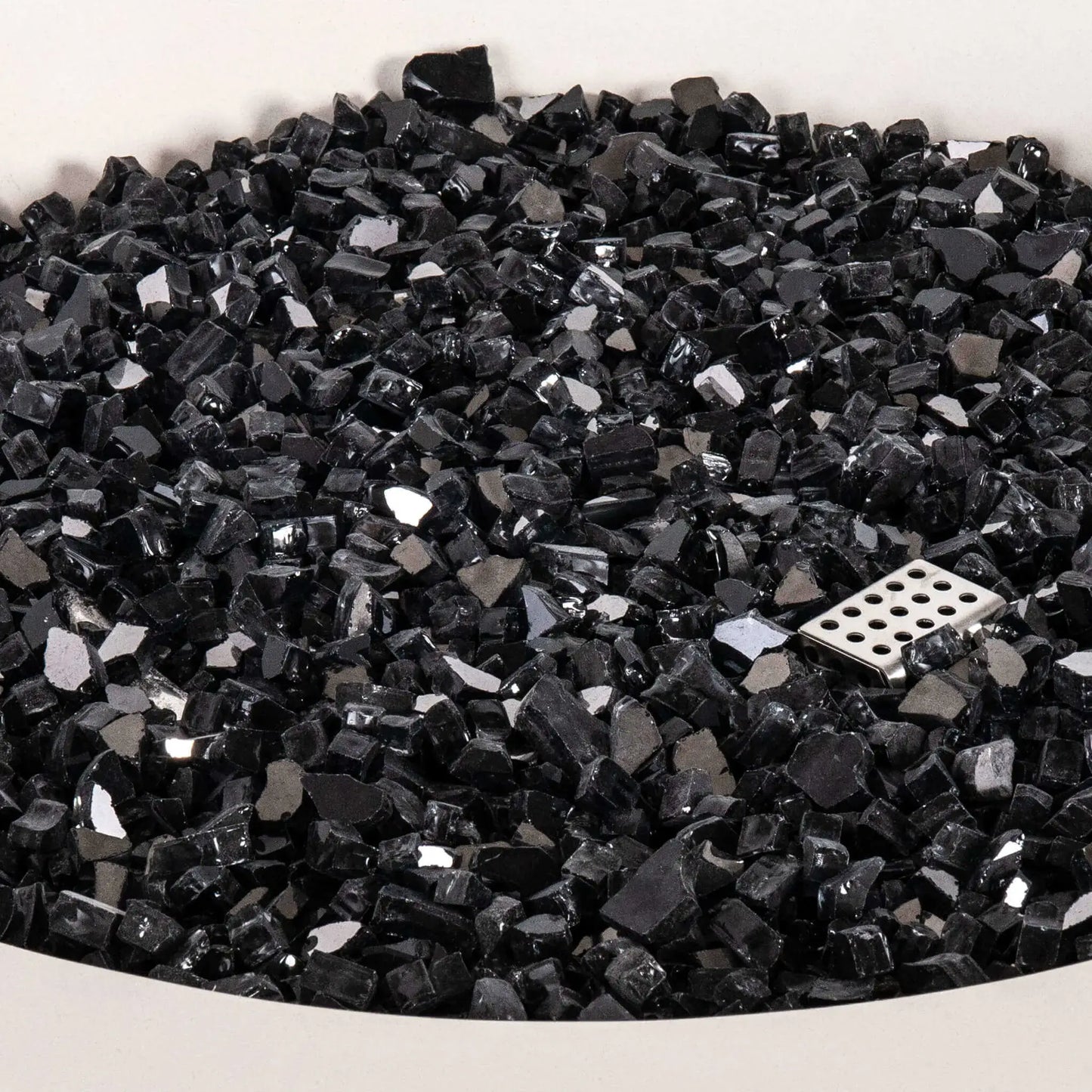 Detailed close-up of the tempered black reflective fire glass inside the Flame Havens Refuge Series 43-inch Round Propane Gas GFRC Concrete Fire Pit in White. The image highlights the premium reflective glass media surrounding the stainless steel CSA ignition component, showcasing the quality, depth, and polished finish of the fire feature.