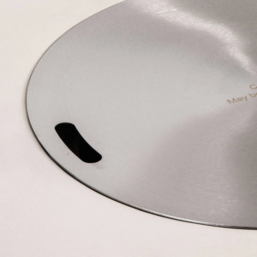 Close-up of the optional stainless steel burner cover for the Flame Havens Refuge Series 43-inch Round Propane Gas GFRC Concrete Fire Pit in White. The precision-finished cover features integrated lift handles and a brushed stainless surface, converting the fire pit into a functional tabletop when the burner is not in use.