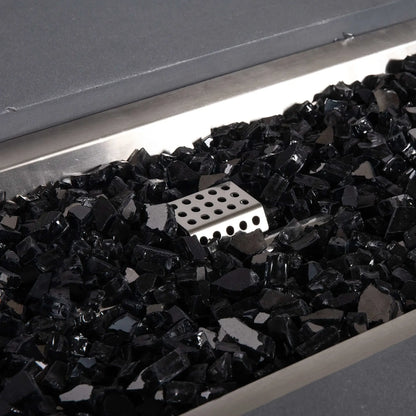 Close-up of the Flame Havens Refuge Series 56 x 30 x 15 inch rectangle natural gas gray fire pit, featuring reflective tempered black fire glass surrounding the stainless steel CSA ignition assembly. The detailed view emphasizes premium materials and the clean burner pan finish.