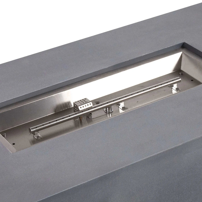 Close-up image of the Flame Havens Refuge Series 56 x 30 x 15 inch rectangle natural gas gray GFRC fire pit showing the stainless steel burner tube, burner pan, and CSA ignition assembly. The image provides a clear look at the premium internal burner components and construction quality.