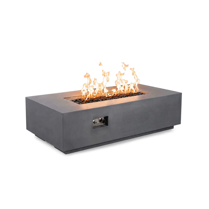 Angled product view of the Flame Havens Refuge Series 56 x 30 x 15 inch rectangle natural gas gray GFRC fire pit featuring reflective tempered black fire glass, vibrant flames, and a recessed front control panel for easy ignition and flame adjustment.