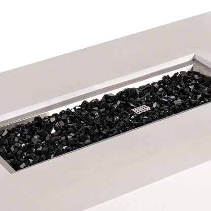 Angled close-up of the Flame Havens Refuge Series 56 x 30 x 15 inch rectangle natural gas white GFRC concrete fire pit showcasing reflective black fire glass neatly filling the brushed stainless steel burner pan. The image highlights the premium fire media, clean rectangular opening, and modern craftsmanship designed for luxury outdoor living.