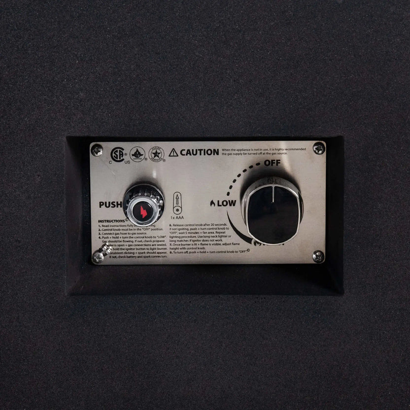 Detailed close-up of the Flame Havens Refuge Series 56 x 30 x 15 inch rectangle natural gas fire pit control panel, highlighting the CSA-certified ignition system, push-button spark igniter, adjustable gas control knob, and stainless steel mounting plate recessed into the black GFRC body.