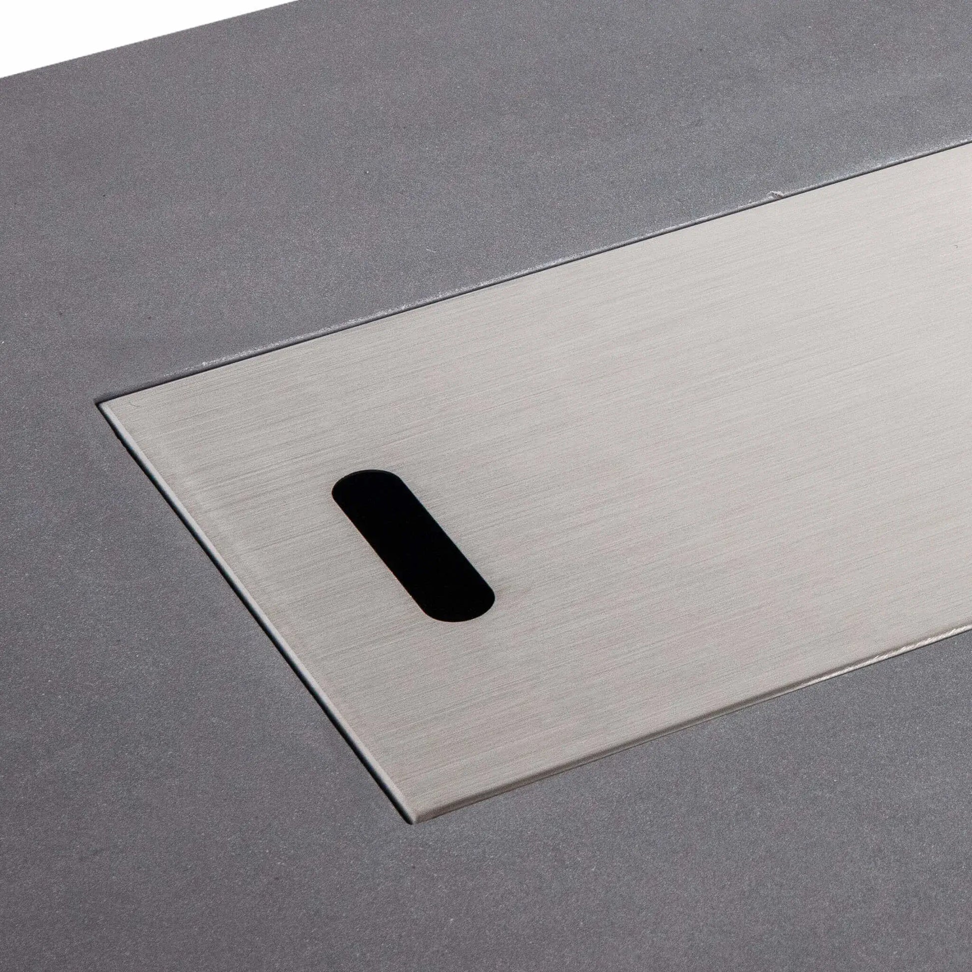 Close-up of the Flame Havens Refuge Series 56 x 30 x 15 inch rectangle natural gas gray GFRC fire pit with the brushed stainless steel burner cover installed. The precision-fit cover sits flush within the burner opening, providing a clean tabletop appearance when the fire feature is not in use.