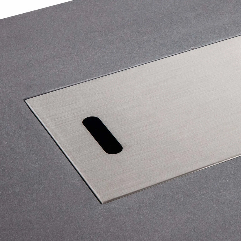 Close-up of the Flame Havens Refuge Series 56 x 30 x 15 inch rectangle natural gas gray GFRC fire pit with the brushed stainless steel burner cover installed. The precision-fit cover sits flush within the burner opening, providing a clean tabletop appearance when the fire feature is not in use.