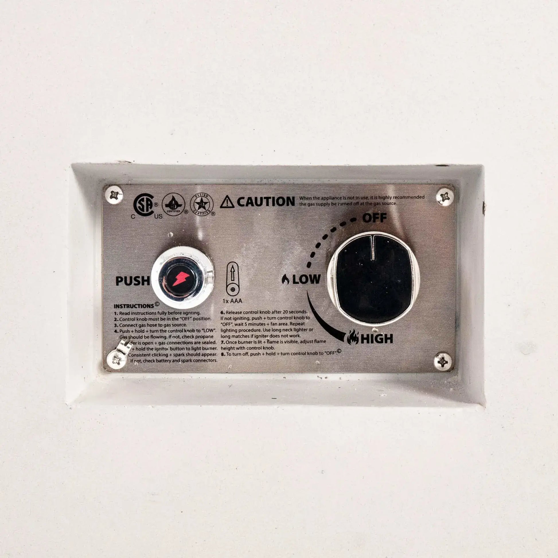 Detailed close-up of the Flame Havens Refuge Series 56 x 30 x 15 inch rectangle natural gas white GFRC concrete fire pit showing the recessed CSA-certified ignition control panel. The stainless steel faceplate features the push-button igniter, flame adjustment knob, operating instructions, and safety markings for reliable natural gas operation.