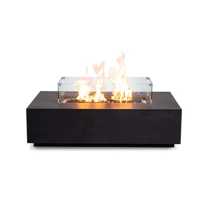 Front-facing product image of the Flame Havens Refuge Series 56 x 30 x 15 inch rectangle natural gas black GFRC fire pit with reflective tempered black fire glass, active flames, tempered glass wind guard, and recessed control panel, combining modern style with enhanced flame protection.