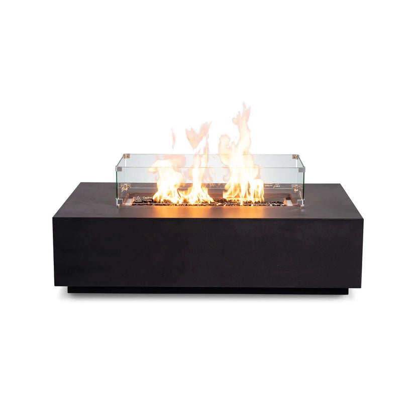 Front-facing product image of the Flame Havens Refuge Series 56 x 30 x 15 inch rectangle natural gas black GFRC fire pit with reflective tempered black fire glass, active flames, tempered glass wind guard, and recessed control panel, combining modern style with enhanced flame protection.