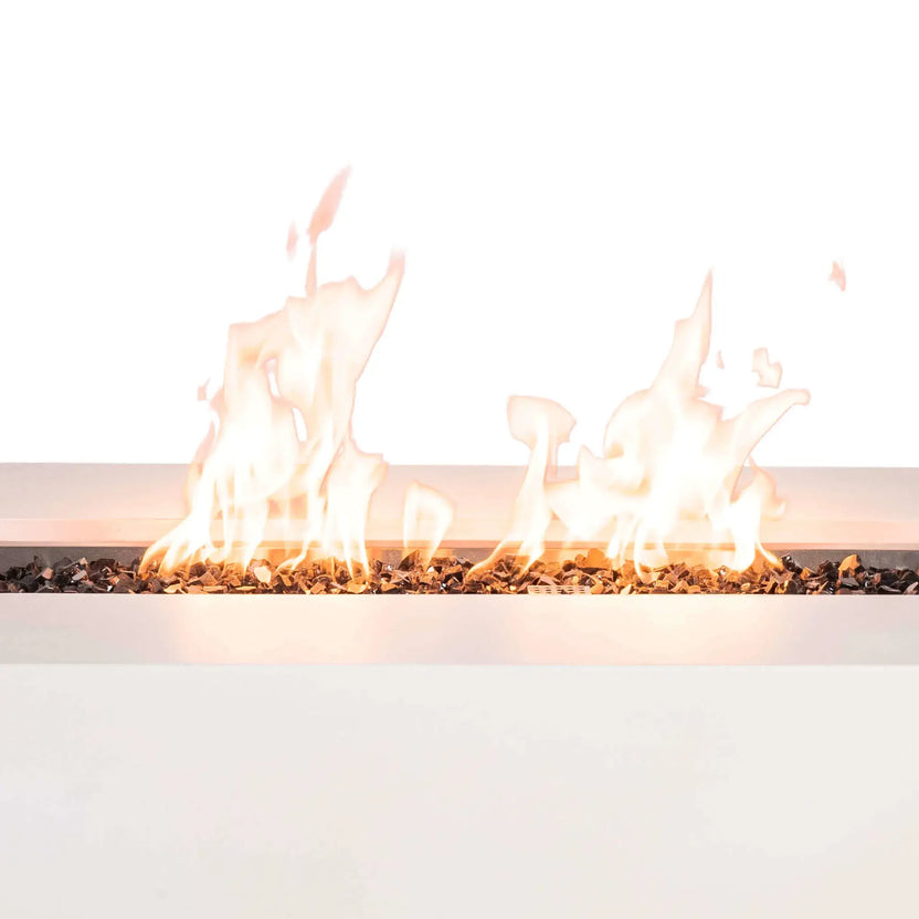Close-up of the Flame Havens Refuge Series 56 x 30 x 15 inch rectangle natural gas white GFRC concrete fire pit showcasing tall, vibrant flames dancing across reflective tempered black fire glass. The linear burner creates an even flame pattern while highlighting the clean contemporary design and premium outdoor fire feature construction.