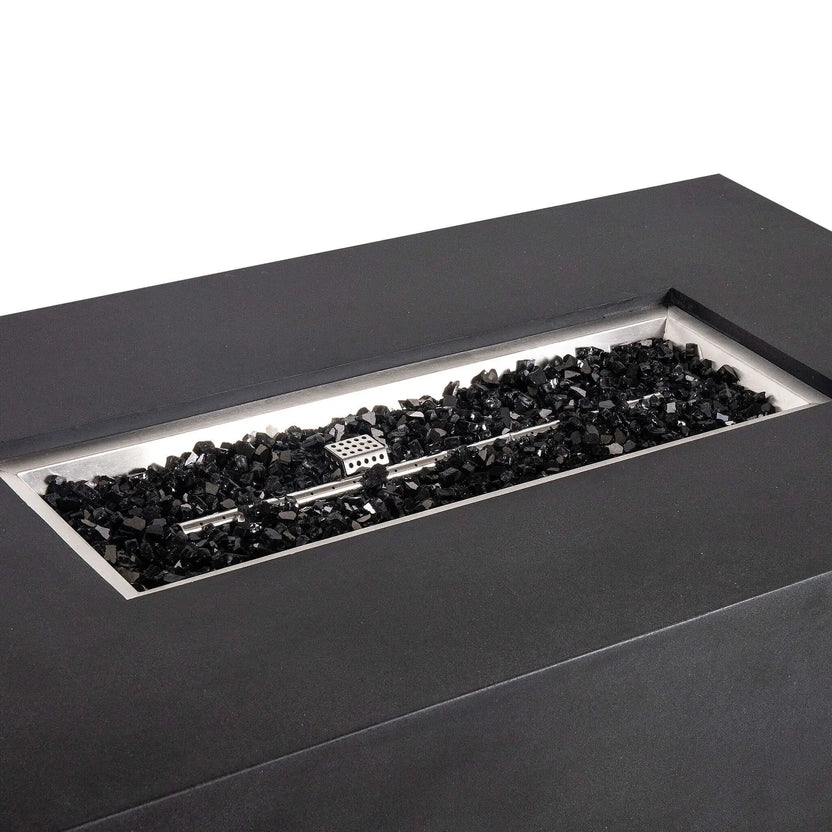 Angled close-up of the black Flame Havens Refuge Series 56 x 30 x 24-inch rectangular GFRC concrete propane gas fire pit, highlighting the recessed stainless steel burner pan, linear burner, protective ignition cage, and glossy black fire glass.