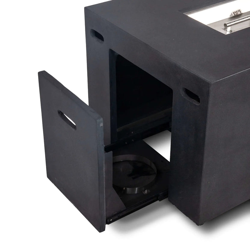 Open hidden propane tank drawer on the black Flame Havens Refuge Series 56 x 30 x 24-inch rectangular GFRC concrete fire pit, showing the empty slide-out tank tray, full-height access door, integrated hand openings, and part of the stainless steel burner above.