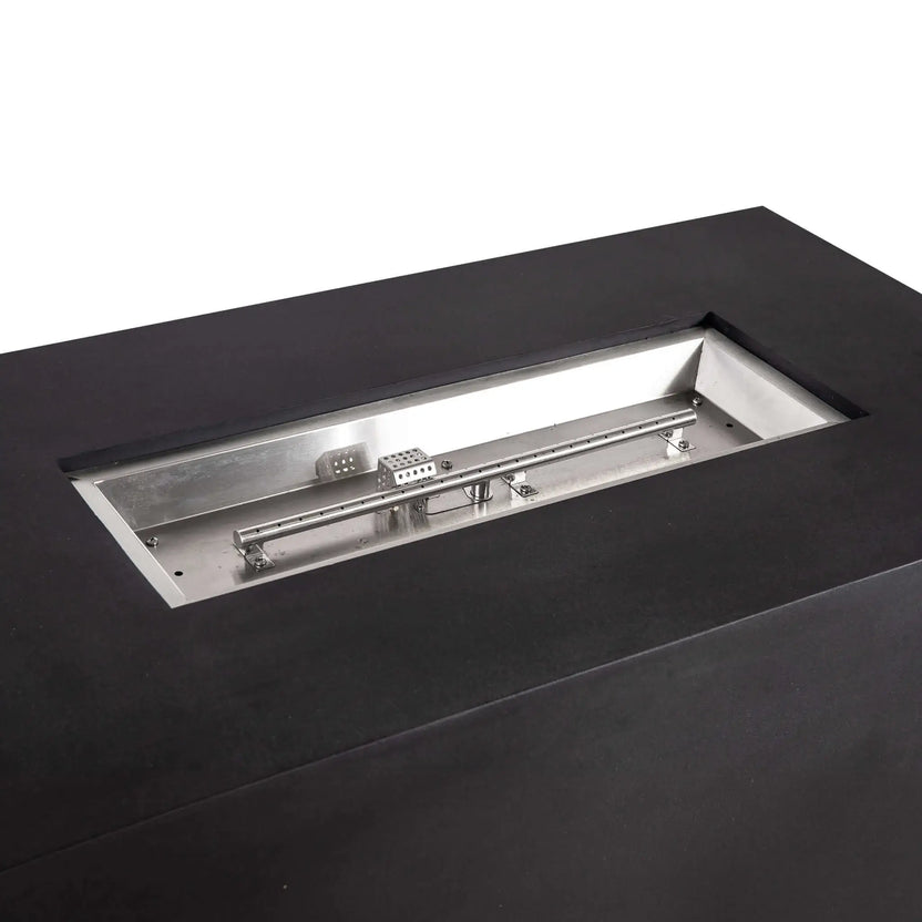 Close-up of the recessed stainless steel burner assembly in the black Flame Havens Refuge Series 56 x 30 x 24-inch rectangular GFRC concrete propane fire pit, showing the linear burner tube, burner ports, mounting hardware, and protected CSA ignition components.