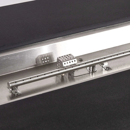 Tight close-up of the Flame Havens Refuge Series propane fire pit’s stainless steel linear burner and CSA ignition system, including evenly spaced burner ports, mounting brackets, wiring, and perforated protective cage set inside the black GFRC concrete surround.