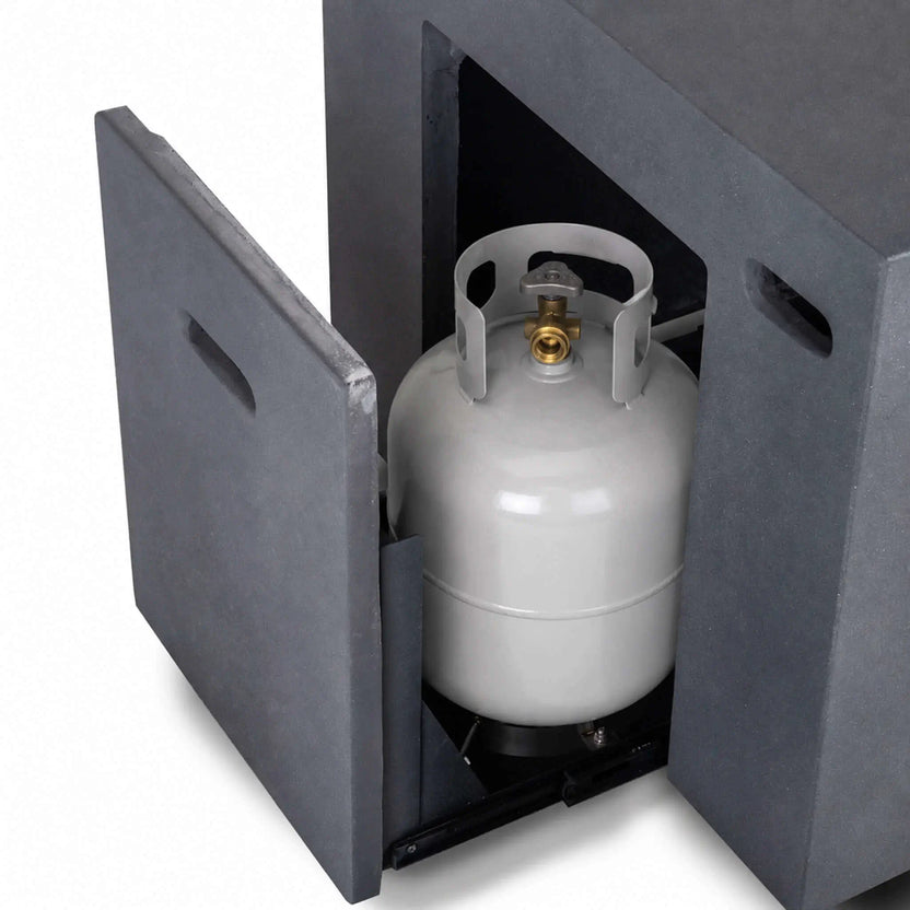 Open hidden propane tank drawer on the Flame Havens Refuge Series 56 x 30 x 24-inch rectangular gray GFRC fire pit, shown with a standard propane cylinder positioned inside. The matching concrete access panel, tank valve, protective collar and sliding support platform are clearly visible.