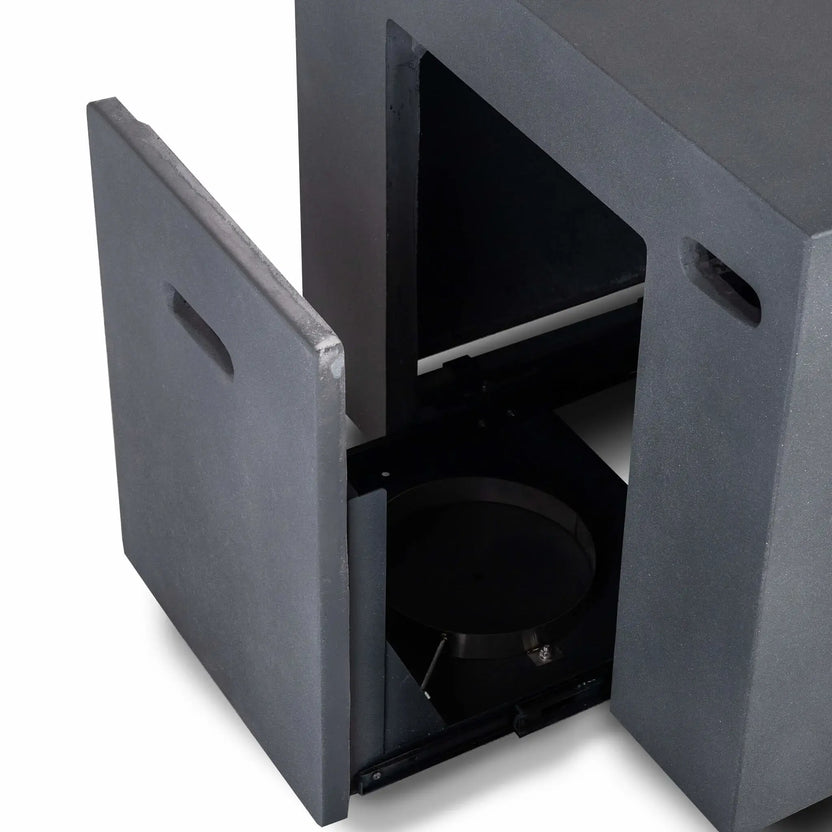 Close-up of the open hidden propane tank drawer on the Flame Havens Refuge Series 56 x 30 x 24-inch rectangular gray GFRC concrete fire pit. The matching concrete access panel opens to reveal the empty interior compartment, circular tank support, sliding base and built-in ventilation openings.
