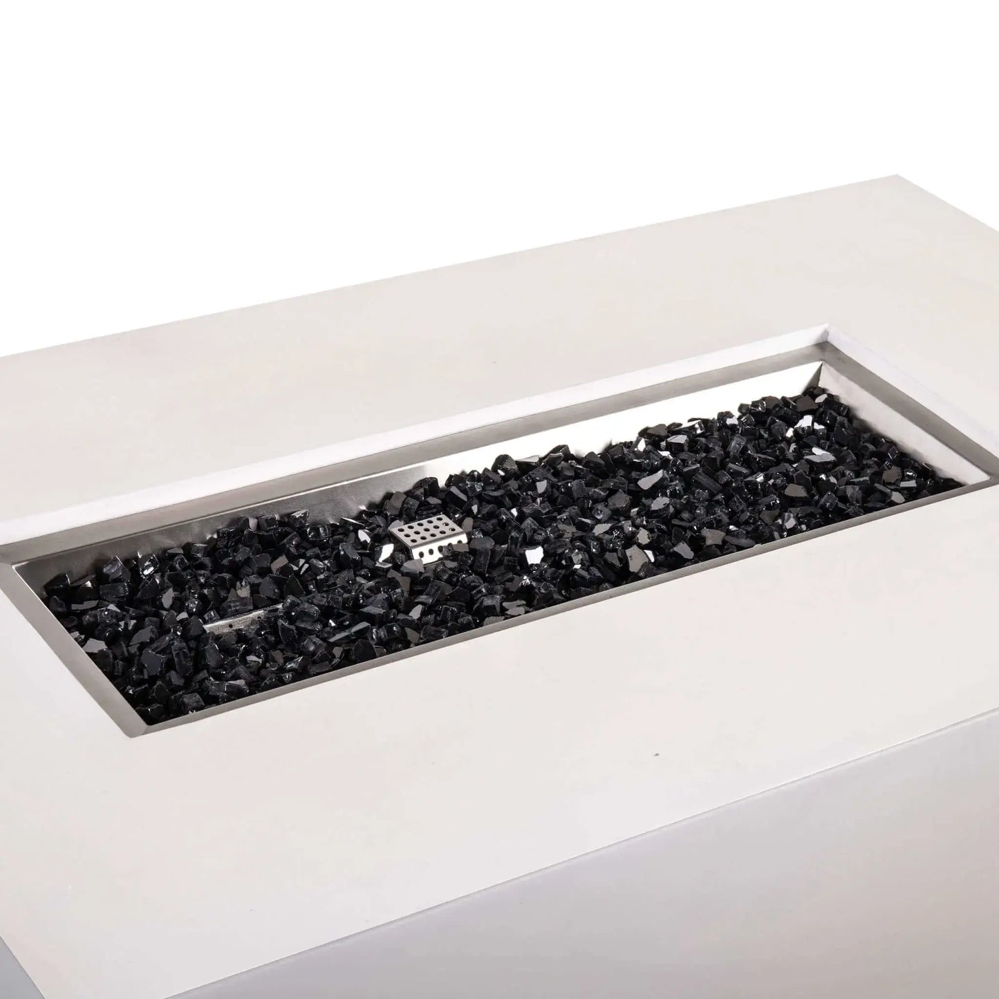 Angled close-up of the Flame Havens Refuge Series 56 x 30 x 24-inch rectangular propane gas fire pit in white GFRC concrete, showing the recessed stainless steel burner pan filled with black reflective fire glass and the central ignition cage.