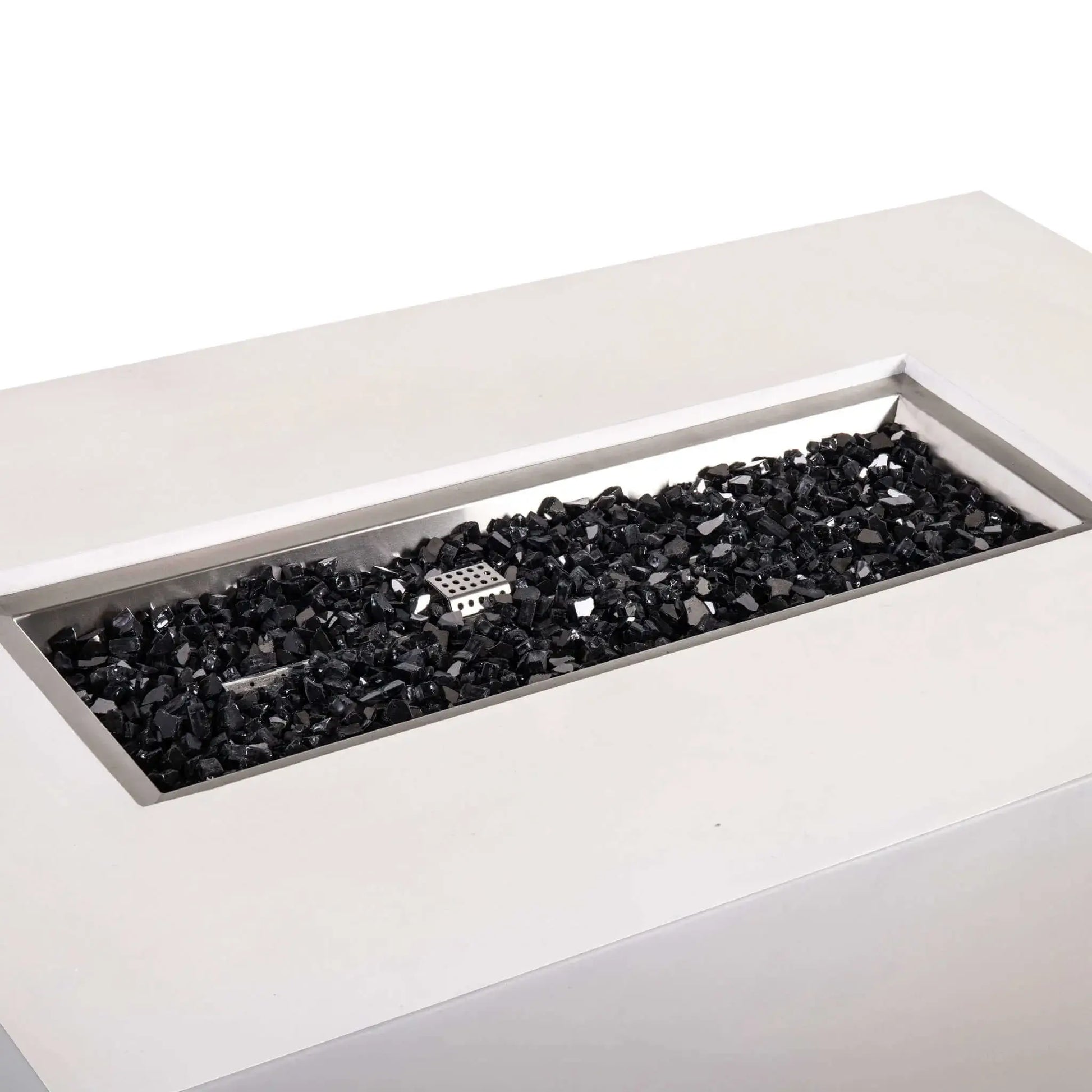 Angled close-up of the Flame Havens Refuge Series 56 x 30 x 24-inch rectangular propane gas fire pit in white GFRC concrete, showing the recessed stainless steel burner pan filled with black reflective fire glass and the central ignition cage.