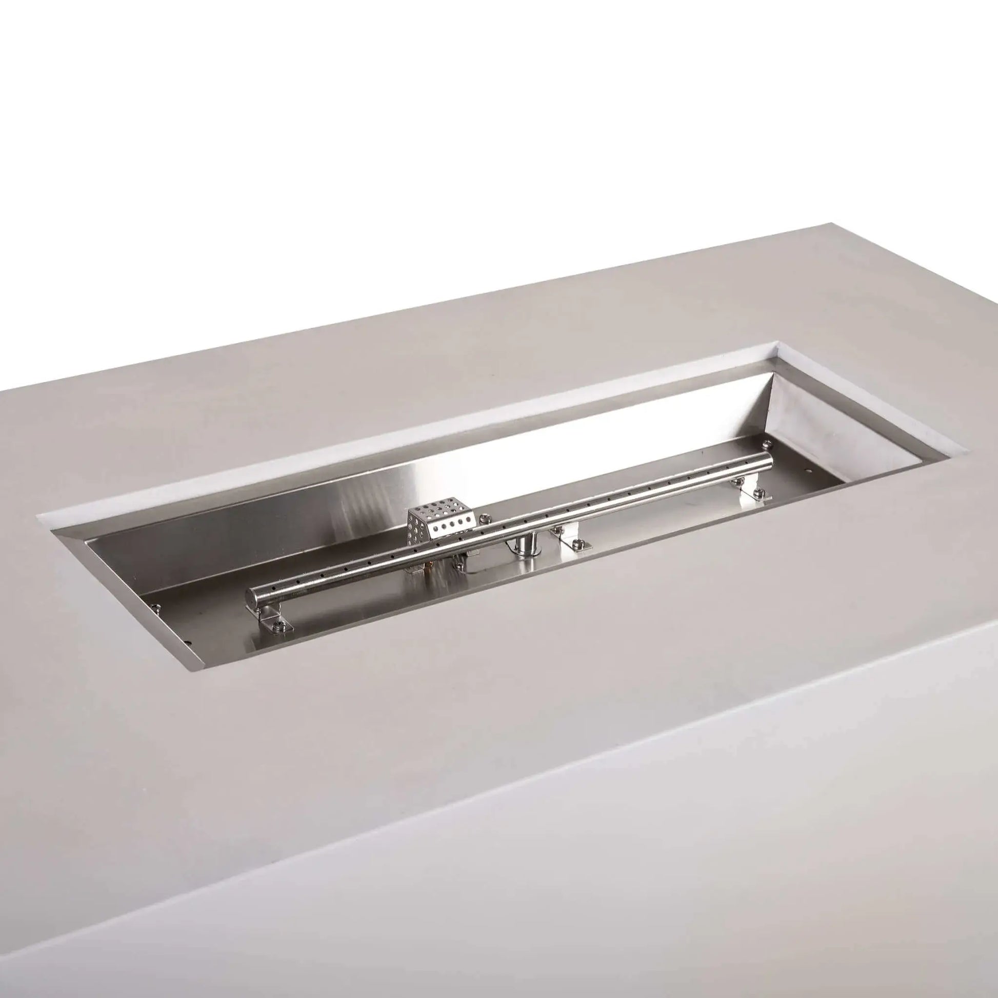 Angled close-up of the stainless steel burner assembly inside a white Flame Havens Refuge Series 56 x 30 x 24-inch rectangular propane gas fire pit, showing the linear burner tube, mounting brackets, polished burner pan, gas fittings, and perforated CSA ignition cage.
