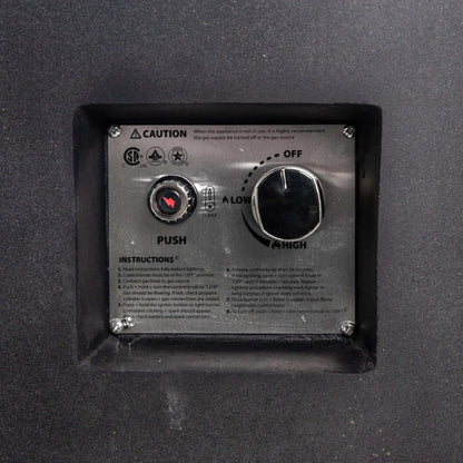 Close-up of the recessed CSA ignition controls on the black Flame Havens Refuge Series rectangular GFRC concrete propane fire pit. The stainless steel panel includes a push-button spark igniter, AAA battery indicator, adjustable control knob with off, low, and high settings, safety notice, and lighting instructions.