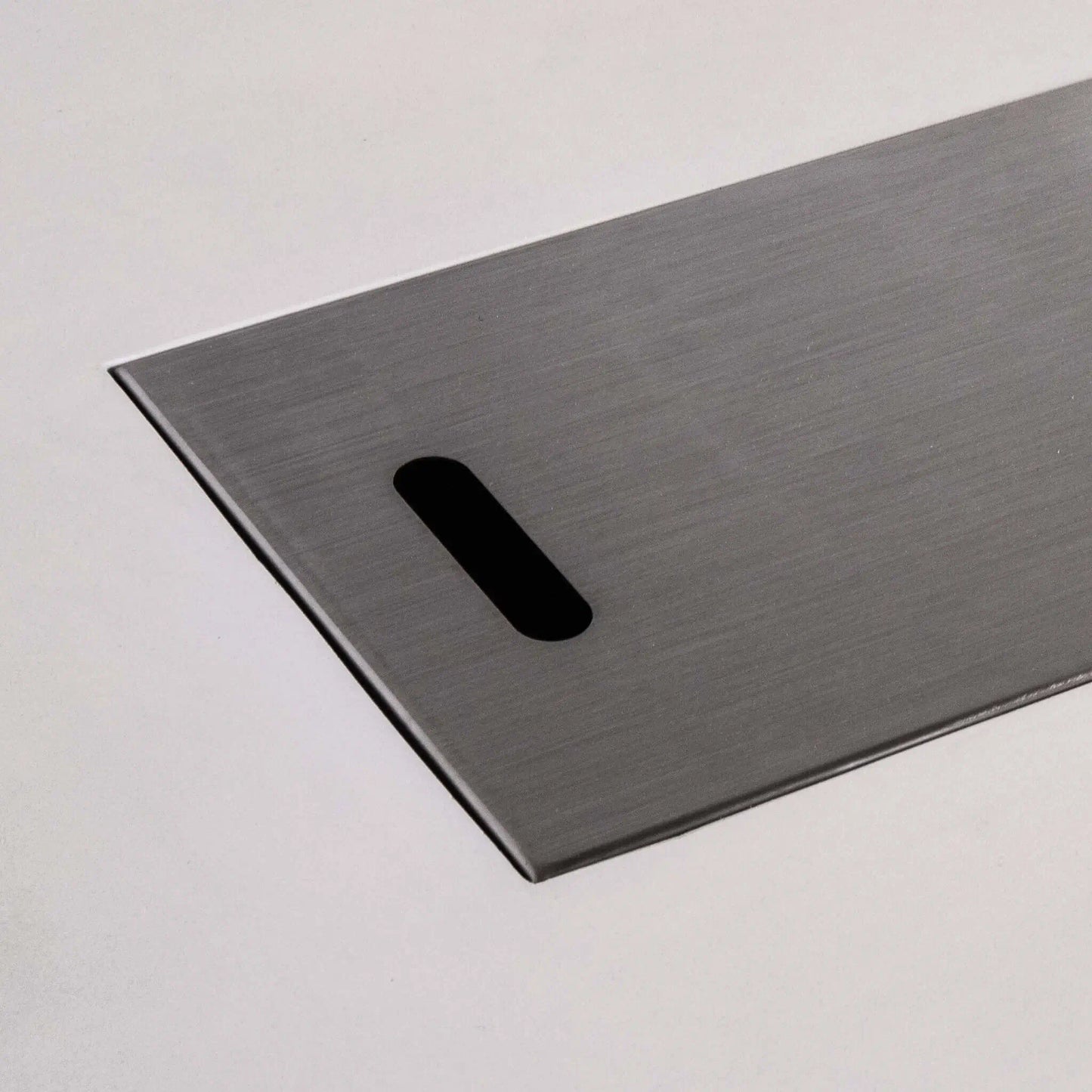 Close-up of the brushed stainless steel burner cover for the white Flame Havens Refuge Series 56 x 30 x 24-inch rectangular propane gas GFRC concrete fire pit, highlighting the smooth metal finish, slim raised edge, and rounded rectangular lifting slot.