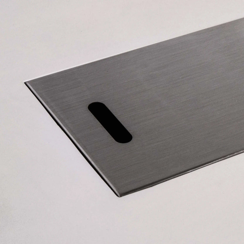 Close-up of the brushed stainless steel burner cover for the white Flame Havens Refuge Series 56 x 30 x 24-inch rectangular propane gas GFRC concrete fire pit, highlighting the smooth metal finish, slim raised edge, and rounded rectangular lifting slot.