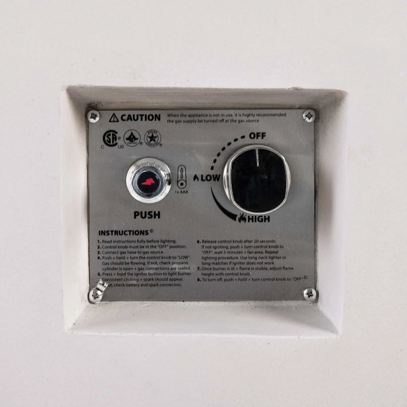 Close-up of the recessed CSA ignition controls on a white Flame Havens Refuge Series 56 x 30 x 24-inch rectangular propane gas fire pit, showing the push-button spark igniter, AAA battery indicator, OFF-to-LOW-to-HIGH flame control knob, safety certifications, caution notice, and lighting instructions.