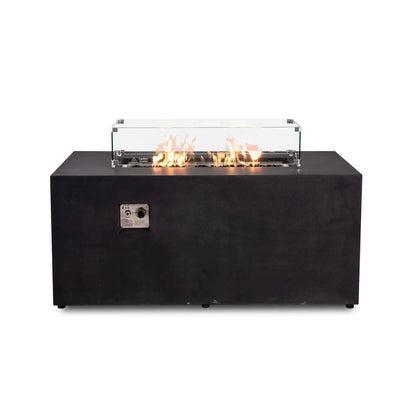 Straight view of the black Flame Havens Refuge Series 56 x 30 x 24-inch rectangular GFRC propane fire pit with an active flame over tempered black fire glass. A clear glass wind guard surrounds the burner and features metal corner brackets, raised feet, and a hot-surface warning.