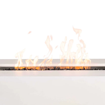 Close-up of the Flame Havens Refuge Series 56 x 30 x 24-inch rectangular white propane gas fire pit burning with tall yellow-orange flames across tempered black fire glass, highlighting the linear burner, stainless steel pan, central ignition cage, and wide white GFRC concrete ledge.