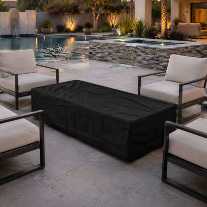 Flame Havens Refuge Series 68 x 30 x 15-inch rectangular fire pit protected by a fitted black canvas fabric cover. The covered fire pit sits between cushioned patio chairs beside a luxury swimming pool and raised spa with a stacked-stone waterfall in a warmly lit outdoor living space.