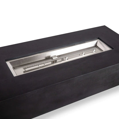 Angled close-up of the Flame Havens Refuge Series black GFRC concrete fire pit with its fire media removed. The open rectangular pan clearly displays the stainless steel natural gas burner assembly, mounting brackets, burner ports, and CSA ignition housing inside the 68 x 30 x 15-inch unit.