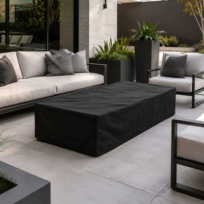 Flame Havens Refuge Series 68 x 30 x 15-inch rectangular GFRC natural gas fire pit protected by a fitted black canvas fabric cover. The covered fire pit is centered within a modern outdoor lounge featuring white cushioned seating, black frames, large planters, and contemporary landscaping.
