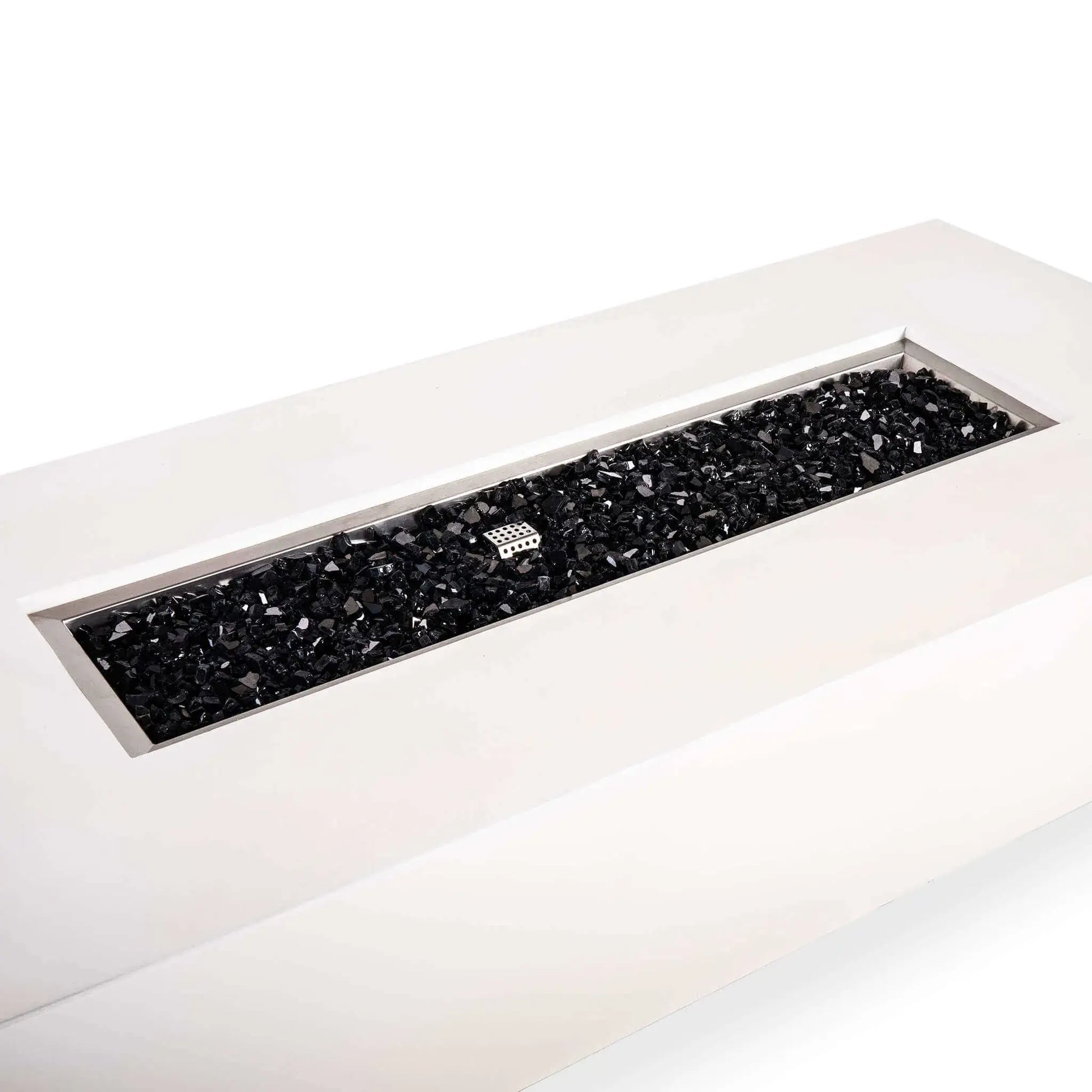 Angled detail of a Flame Havens Refuge Series 68 x 30 x 15-inch rectangular natural gas fire pit in white GFRC concrete. The long stainless steel burner pan is filled with reflective tempered black fire glass, with a perforated ignition cage visible near the center and a broad, smooth concrete ledge surrounding the opening.