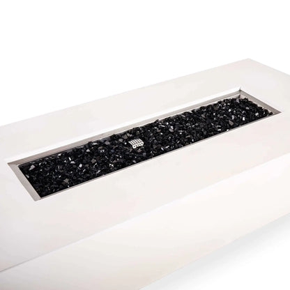 Angled detail of a Flame Havens Refuge Series 68 x 30 x 15-inch rectangular natural gas fire pit in white GFRC concrete. The long stainless steel burner pan is filled with reflective tempered black fire glass, with a perforated ignition cage visible near the center and a broad, smooth concrete ledge surrounding the opening.