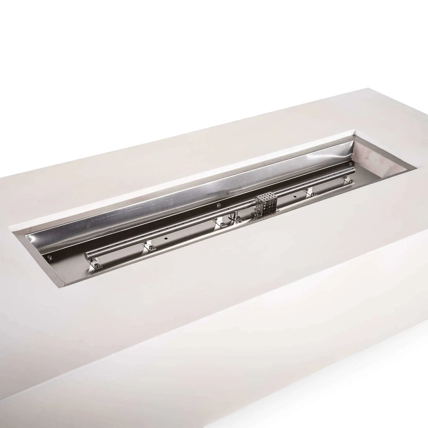 Close-up angled view of the Flame Havens Refuge Series white GFRC natural gas fire pit, showcasing its long stainless steel burner pan before fire glass is added. The linear burner tube, mounting brackets, ignition components and perforated CSA ignition cage are clearly visible within the 68-inch rectangular fire pit.