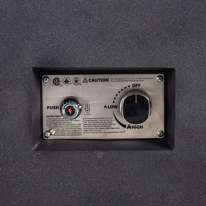 Close-up of the recessed CSA ignition controls on the Flame Havens Refuge Series 68 x 30 x 15-inch rectangular natural gas fire pit. The stainless steel panel includes a push-button spark igniter, AAA battery indicator, operating instructions, safety markings, and a large flame-control knob labeled off, low, and high.
