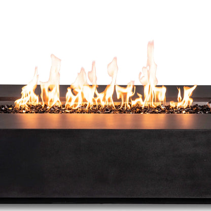 Close-up of active natural gas flames stretching across reflective tempered black fire glass in the Flame Havens Refuge Series 68 x 30 x 15-inch rectangular fire pit. The image highlights the varied flame heights, stainless steel burner-pan edge, dark GFRC concrete finish, and concealed-control design.