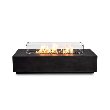 Straight-on product view of the Flame Havens Refuge Series 68 x 30 x 15-inch black GFRC natural gas fire pit with no exterior controls visible. A clear tempered glass wind guard with metal corner brackets surrounds bright flames burning across reflective tempered black fire glass.