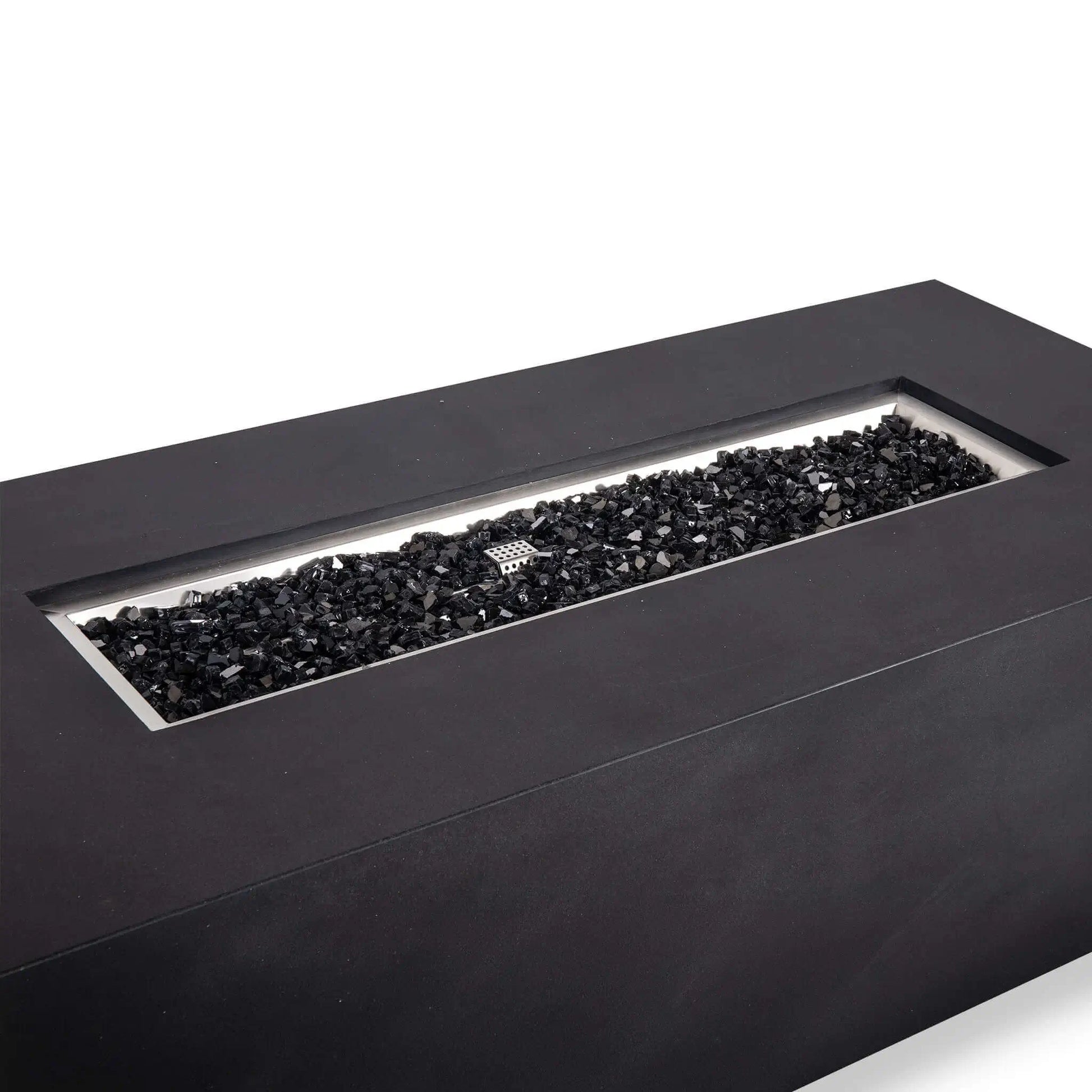 Angled close-up of the black Flame Havens Refuge Series 68 x 30 x 24-inch rectangular GFRC concrete propane gas fire pit, showing the recessed stainless steel burner pan filled with reflective black tempered fire glass and the ignition cage centered among the glass.