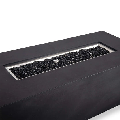 Angled close-up of the black Flame Havens Refuge Series 68 x 30 x 24-inch rectangular GFRC concrete propane gas fire pit, showing the recessed stainless steel burner pan filled with reflective black tempered fire glass and the ignition cage centered among the glass.
