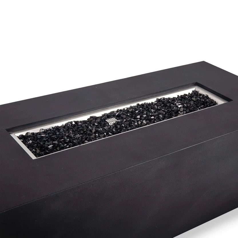 Angled close-up of the black Flame Havens Refuge Series 68 x 30 x 24-inch rectangular GFRC concrete propane gas fire pit, showing the recessed stainless steel burner pan filled with reflective black tempered fire glass and the ignition cage centered among the glass.