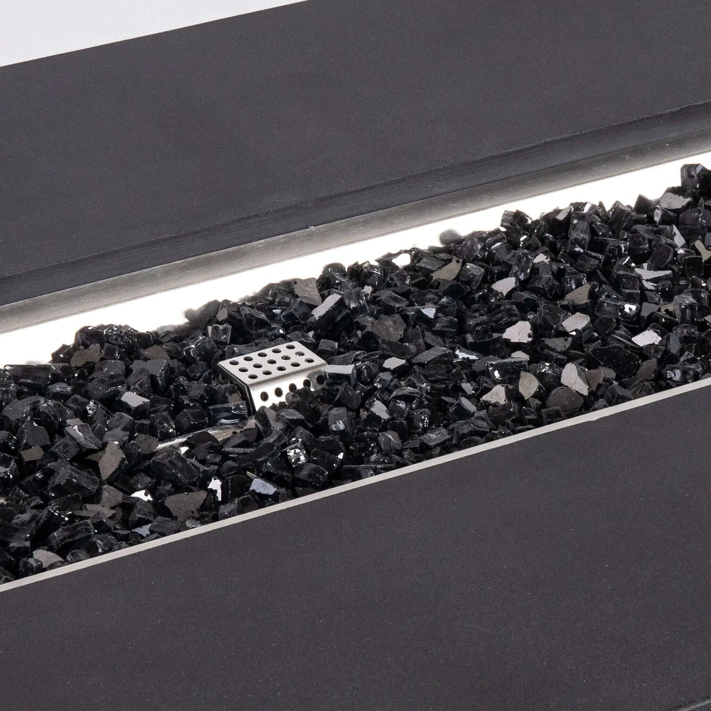 Detailed close-up of reflective black tempered fire glass inside the Flame Havens Refuge Series 68 x 30 x 24-inch rectangular black GFRC concrete propane fire pit, with the stainless steel ignition cage visible among the glossy glass pieces and the burner pan trim framing the opening.