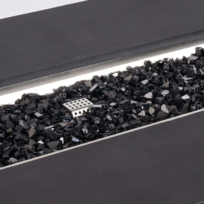 Detailed close-up of reflective black tempered fire glass inside the Flame Havens Refuge Series 68 x 30 x 24-inch rectangular black GFRC concrete propane fire pit, with the stainless steel ignition cage visible among the glossy glass pieces and the burner pan trim framing the opening.