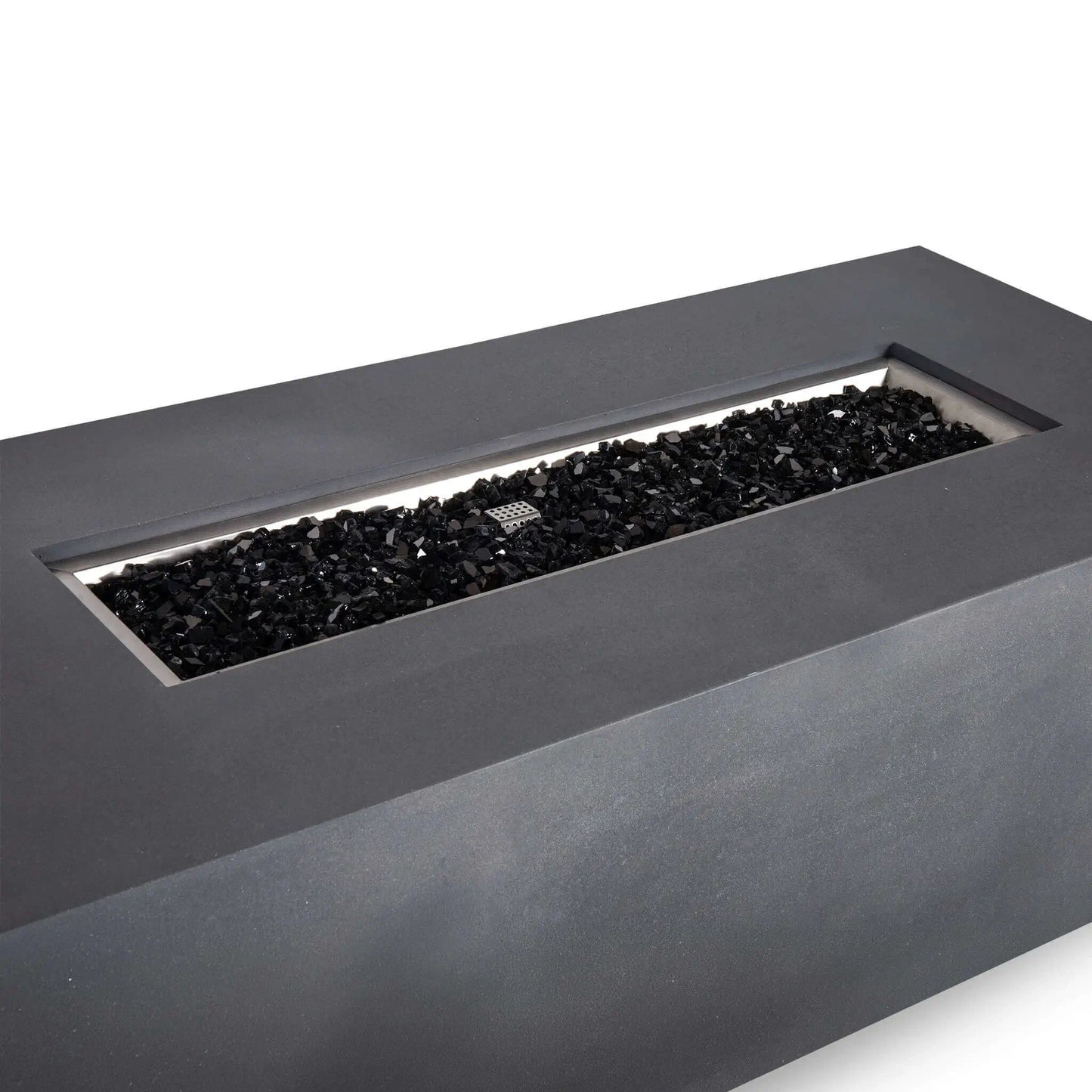 Angled close-up of the Flame Havens Refuge Series 68 x 30 x 24-inch rectangular propane gas fire pit in gray GFRC concrete, featuring a long stainless steel burner pan filled with reflective black fire glass and a visible ignition cage.