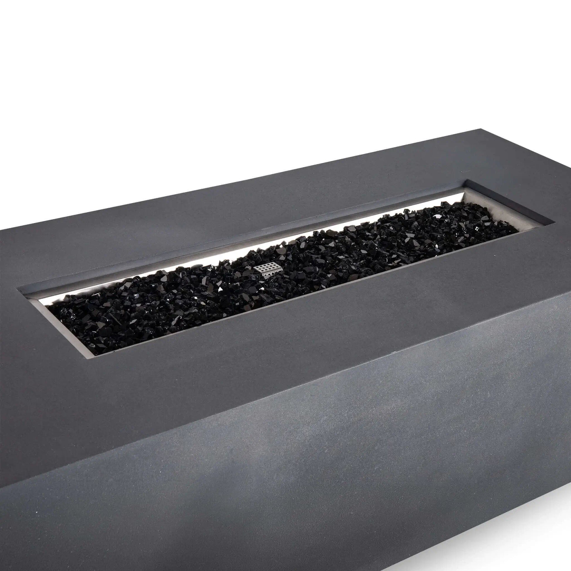 Angled close-up of the Flame Havens Refuge Series 68 x 30 x 24-inch rectangular propane gas fire pit in gray GFRC concrete, featuring a long stainless steel burner pan filled with reflective black fire glass and a visible ignition cage.