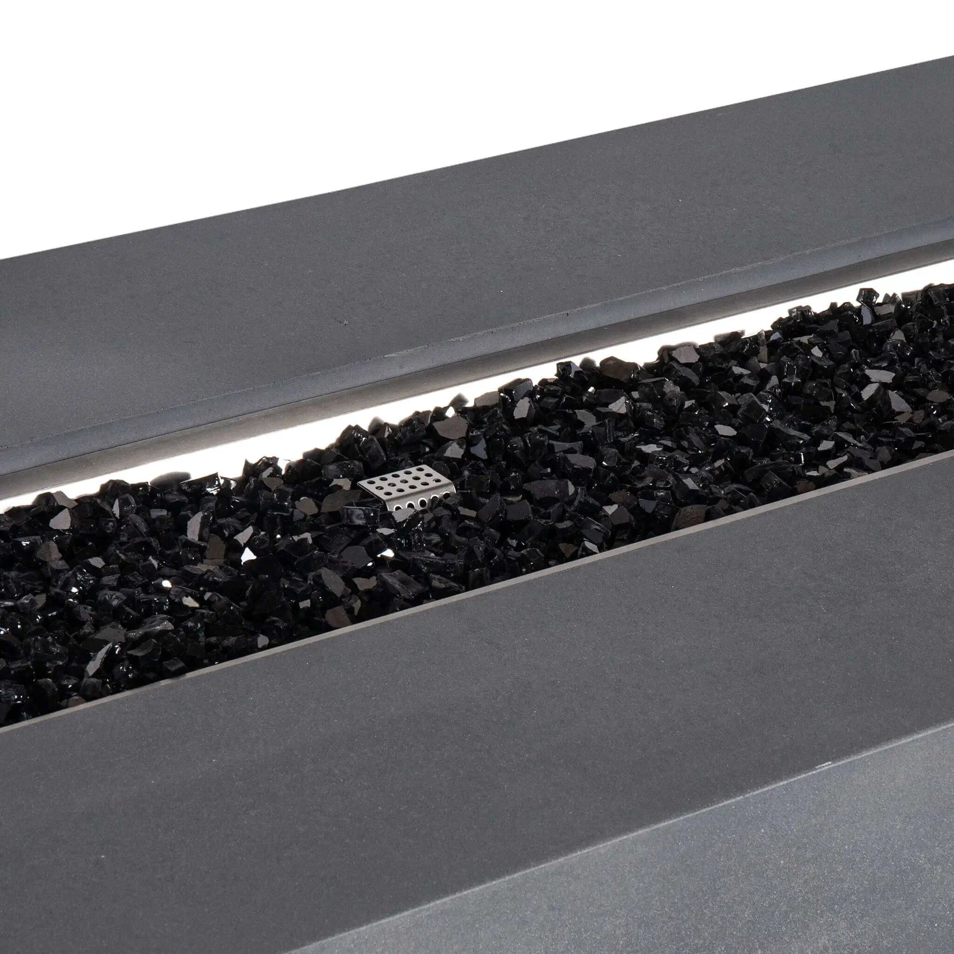 Detailed close-up of the Flame Havens Refuge Series 68 x 30 x 24-inch gray GFRC concrete propane fire pit, showing glossy black reflective fire glass spread across the linear stainless steel burner pan with the perforated ignition cage visible near the center.